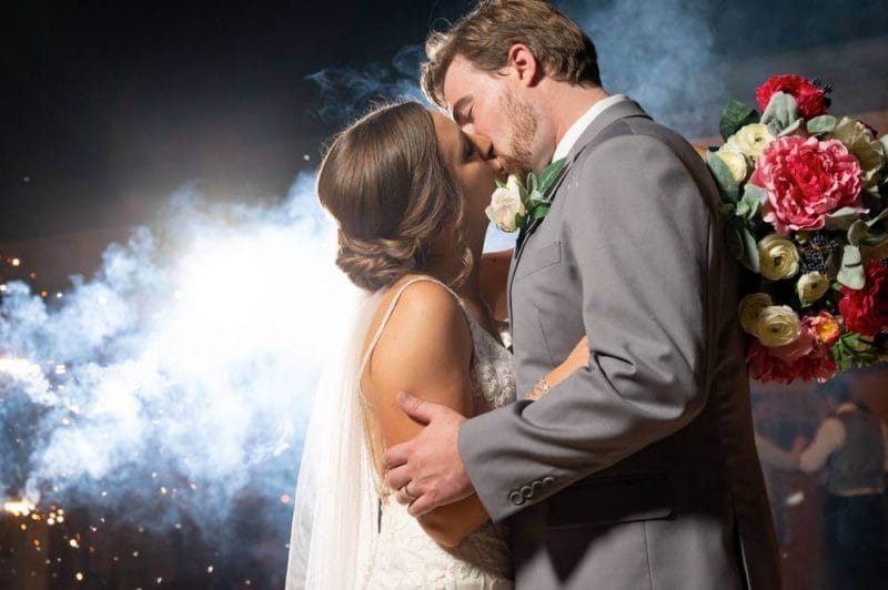 bride and groom kissing with smoke in background from sparklers