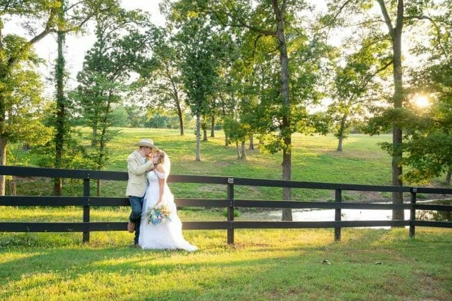 wide shot of bride and groom against a fence with sunset